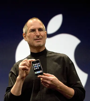 Steve Jobs holding the first iPhone in front of an Apple logo